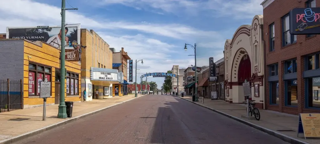 Beale Street in Memphis on a sunny afternoon, with historic storefronts and signs along a brick-paved street