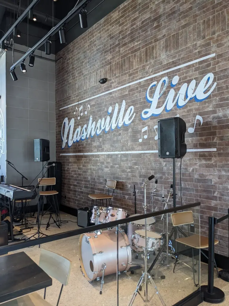 A small live-music stage with a drum kit and a Nashville Live sign on a brick wall inside the BNA airport terminal