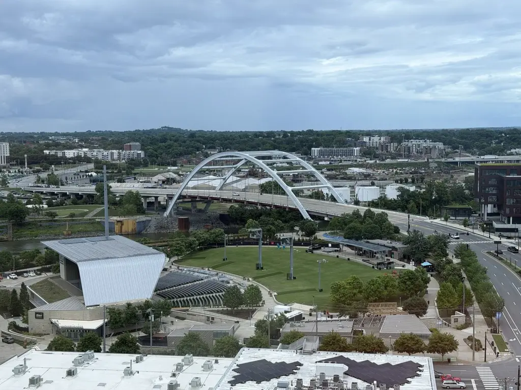 Ascend Amphitheater's stage canopy and lawn beside the Cumberland River with an arched bridge behind, seen from above