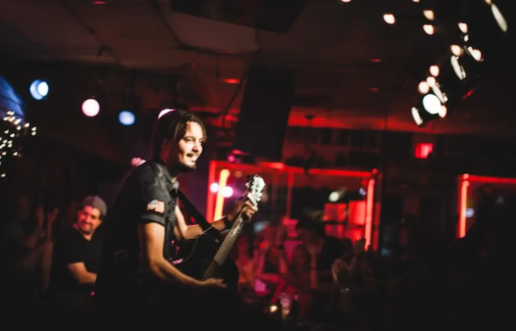 A singer with a guitar performing under red and blue lights inside the Bluebird Cafe