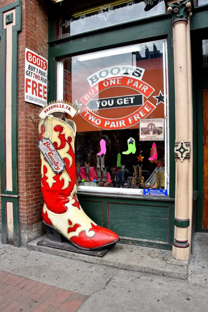A boot shop window with a giant red cowboy boot and a buy one pair, get two free sign
