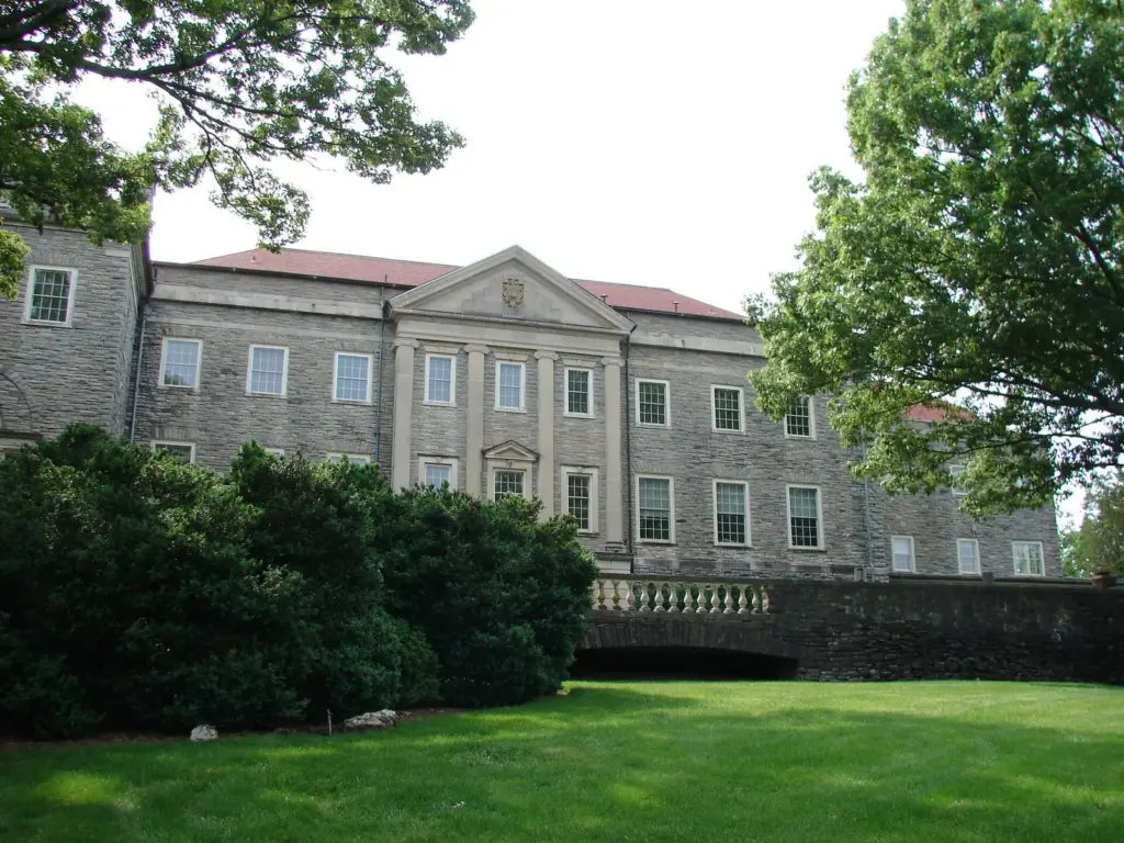 The gray stone Cheekwood mansion seen across a green lawn framed by trees and shrubs