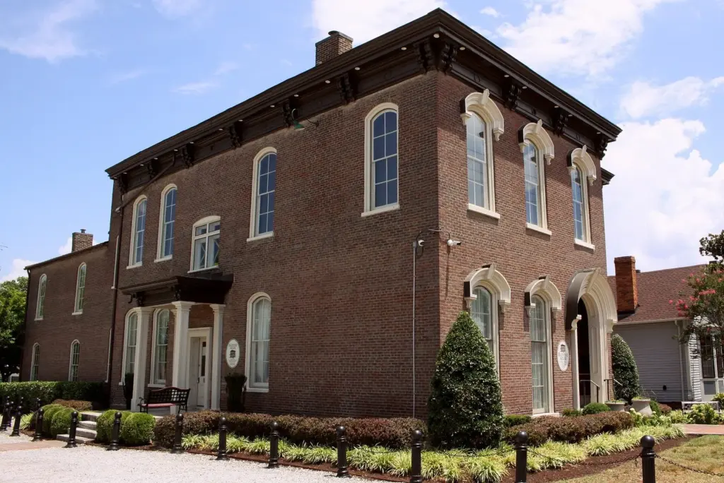 A two-story red brick Italianate house with arched windows and a gravel forecourt