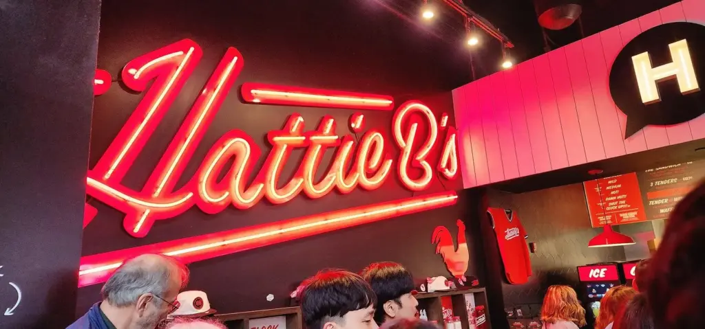 The red neon Hattie B's sign glowing above diners at one of the best restaurants in Nashville for hot chicken, on Lower Broadway