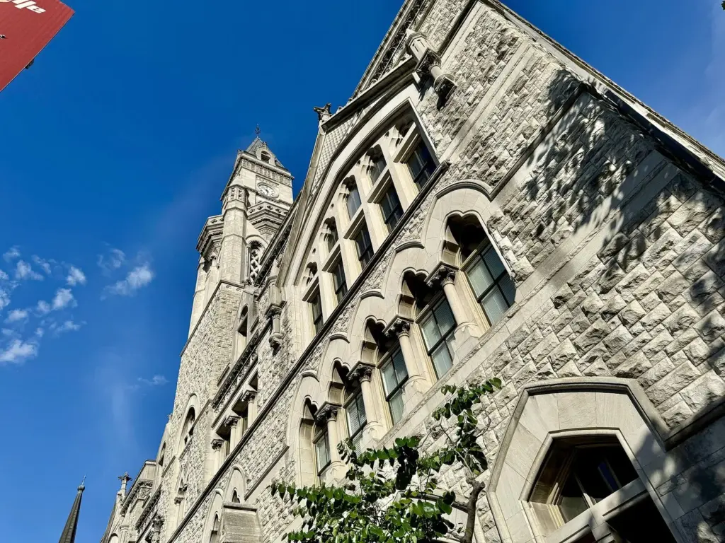 The Victorian Gothic stone Old Customs House with its tall clock tower at Broadway and Seventh Avenue under a deep blue sky