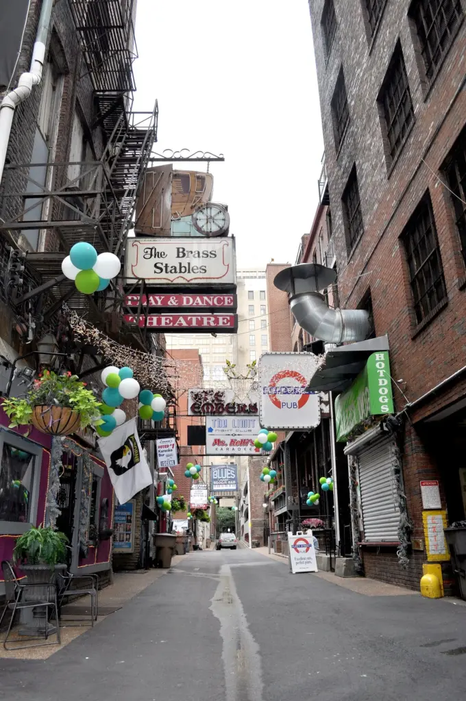 Looking down narrow Printers Alley between brick buildings hung with bar signs and balloons
