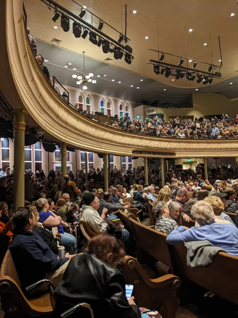 The Ryman Auditorium's curved balcony and wooden pews during a concert