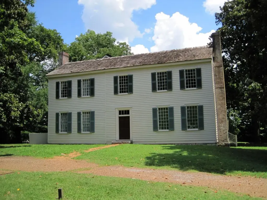 The white two-story clapboard house at Travellers Rest with dark shutters and a stone chimney under a blue sky