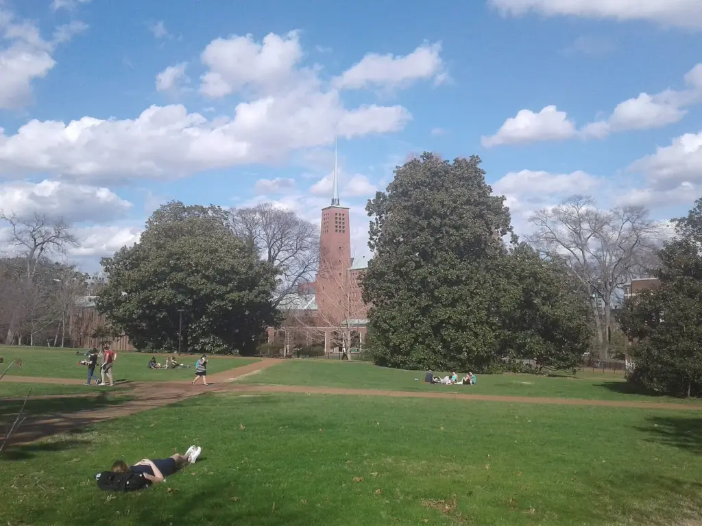 Students relaxing on a wide lawn on Vanderbilt University's campus with a tall brick tower rising behind magnolia trees