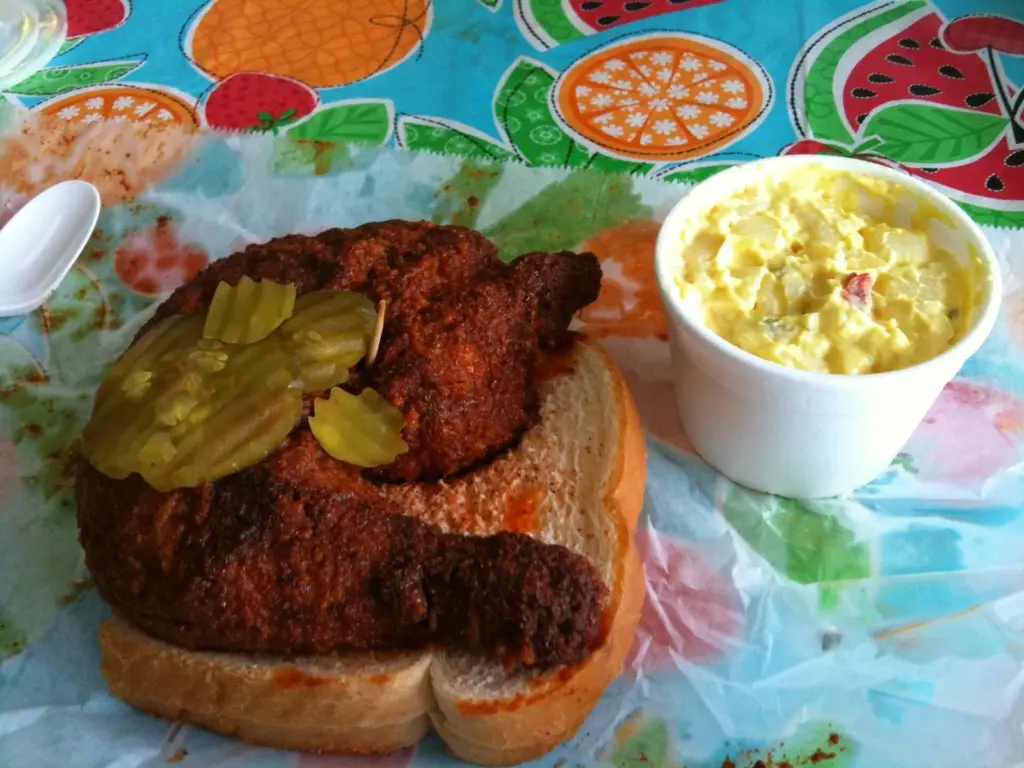 Prince's hot chicken on white bread with pickle chips and a cup of potato salad