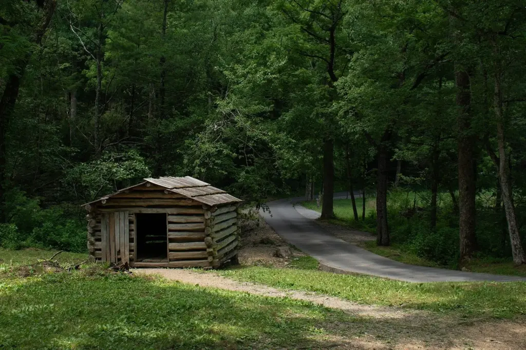 A small weathered log building beside a path under tall trees at Tipton Place in Cades Cove