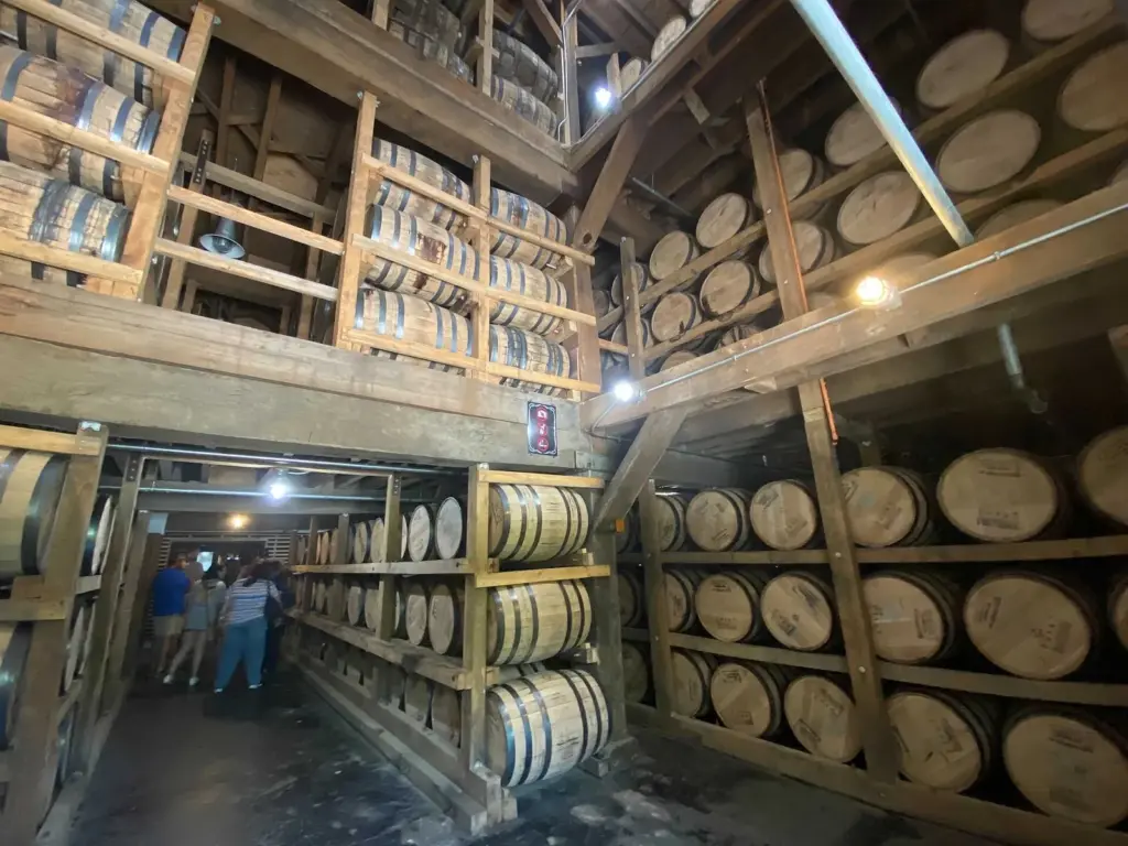 Rows of whiskey barrels stacked on wooden racks several stories high inside a Jack Daniel's barrelhouse, with a tour group walking between them