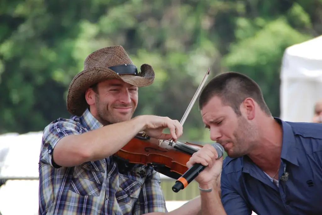 A fiddler and a singer in a cowboy hat performing on an outdoor fan stage at CMA Fest