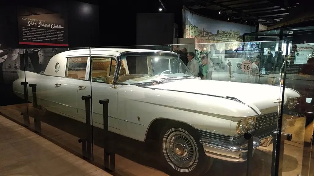 Elvis Presley's white Cadillac limousine with gold-plated trim behind glass in a museum gallery