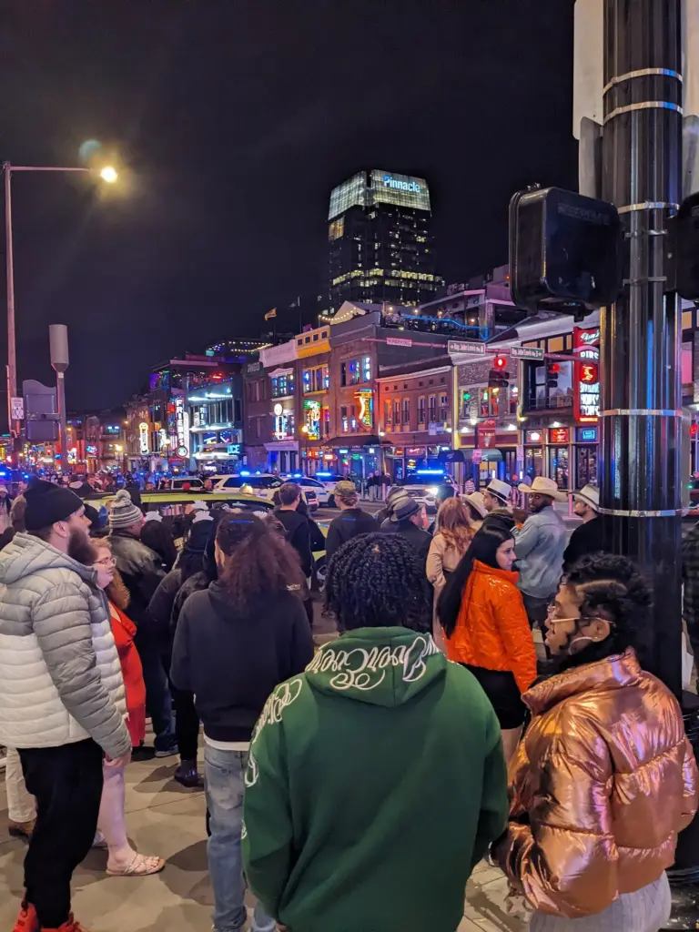 Crowds in winter coats on a sidewalk on Lower Broadway on New Year's Eve, with neon signs behind